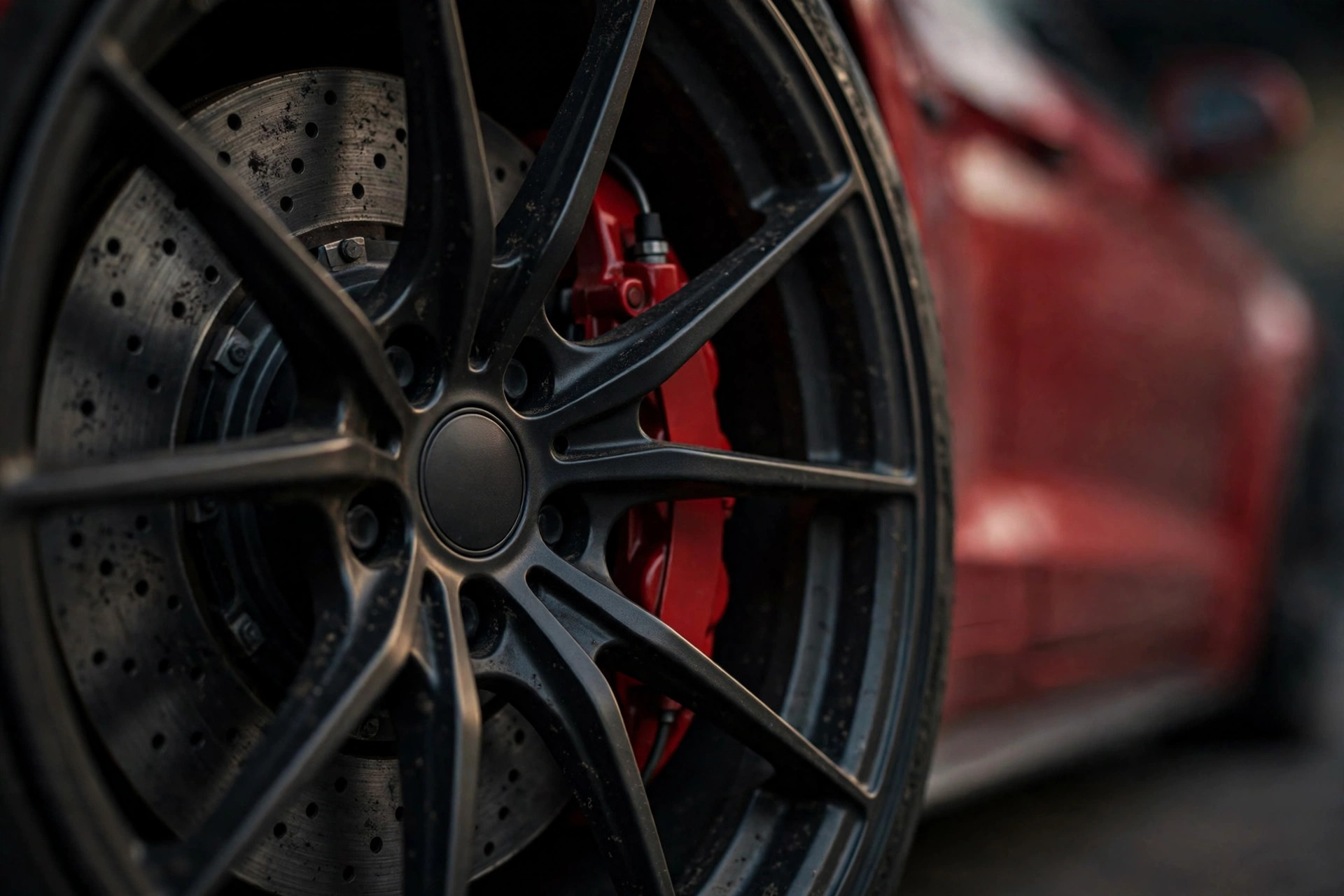 Close-up of a dark alloy wheel with drilled brake disc and red caliper, no logos visible